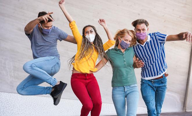 Young people having fun around city street during coronavirus outbreak - Happy friends wearing face protective masks and laughing together - Main focus on girls faces